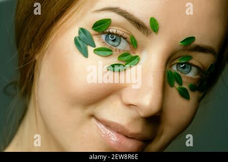 Nahaufnahme`s Gesicht einer jungen Frau mit Buchsbaumblättern. Spa und Wellness Konzept Vorlage Banner für Design. Werbung für kosmetische Produkte Stockfoto